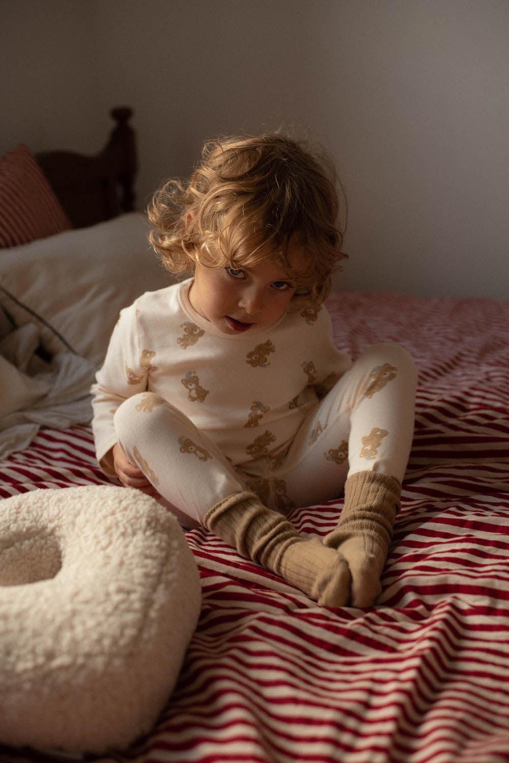 little boy sitting on bed next to boucle pillow by bettys home